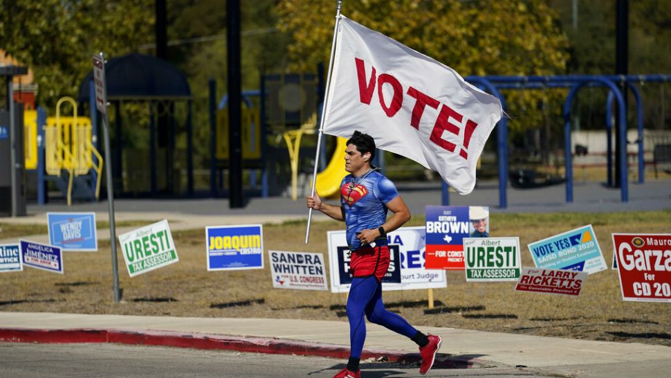 A jogger carries a Vote! flag as he passes a polling station, Tuesday, Nov. 3, 2020, in San Antonio. (AP Photo/Eric Gay)