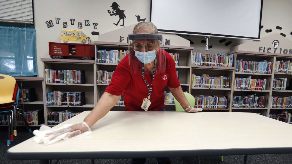 Wearing a mask and face guard as protection against the spread of COVID-19, Garland Independent School District custodian Camelia Tobon wipes down a table in the library at Stephens Elementary School in Rowlett, Texas, Wednesday, July 22, 2020.(AP Photo/LM Otero)