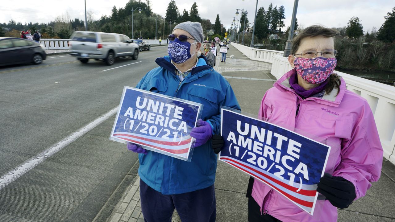 People hold signs that read "Unite America" during a vigil supporting a peaceful transition from President Donald Trump to President-elect Joe Biden, Monday, Jan. 18, 2021, in Olympia, Wash. (AP Photo/Ted S. Warren)