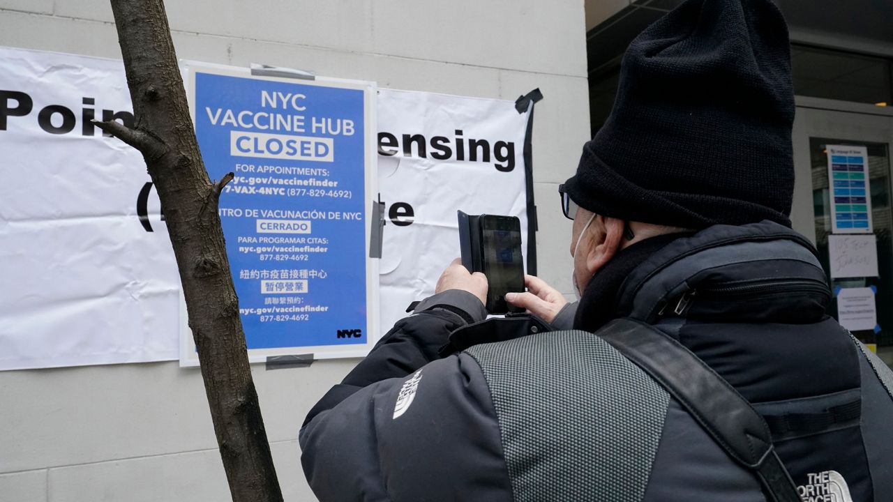 A man takes a cell phone photo of a sign posted outside a Brooklyn COVID-19 vaccine hub that was closed due a shortage in vaccine supply, Thursday, Jan. 21, 2021, in New York, after he tried to enter the building but found it locked.
