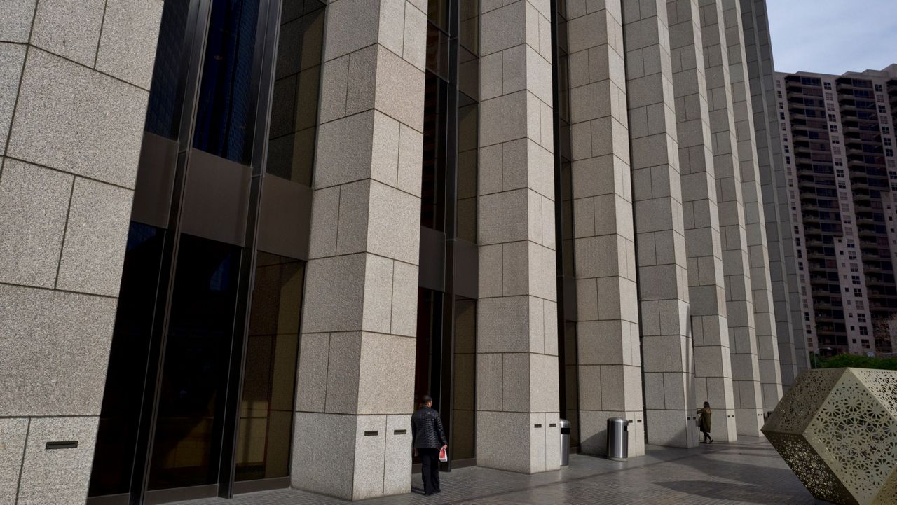 In this Jan. 8, 2019 photo people are towered by the front facade of the Bank of America Plaza Building in downtown Los Angeles. (AP Photo/Richard Vogel, File)