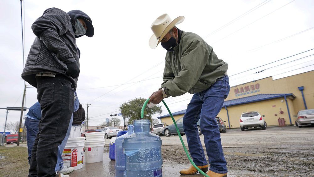 Leovardo Perez, right, fills a water jug using a hose from a public park water spigot Thursday, Feb. 18, 2021, in Houston. Texas officials have ordered 7 million people to boil tap water before drinking it following days of record low temperatures that damaged infrastructure and froze pipes.(AP Photo/David J. Phillip)