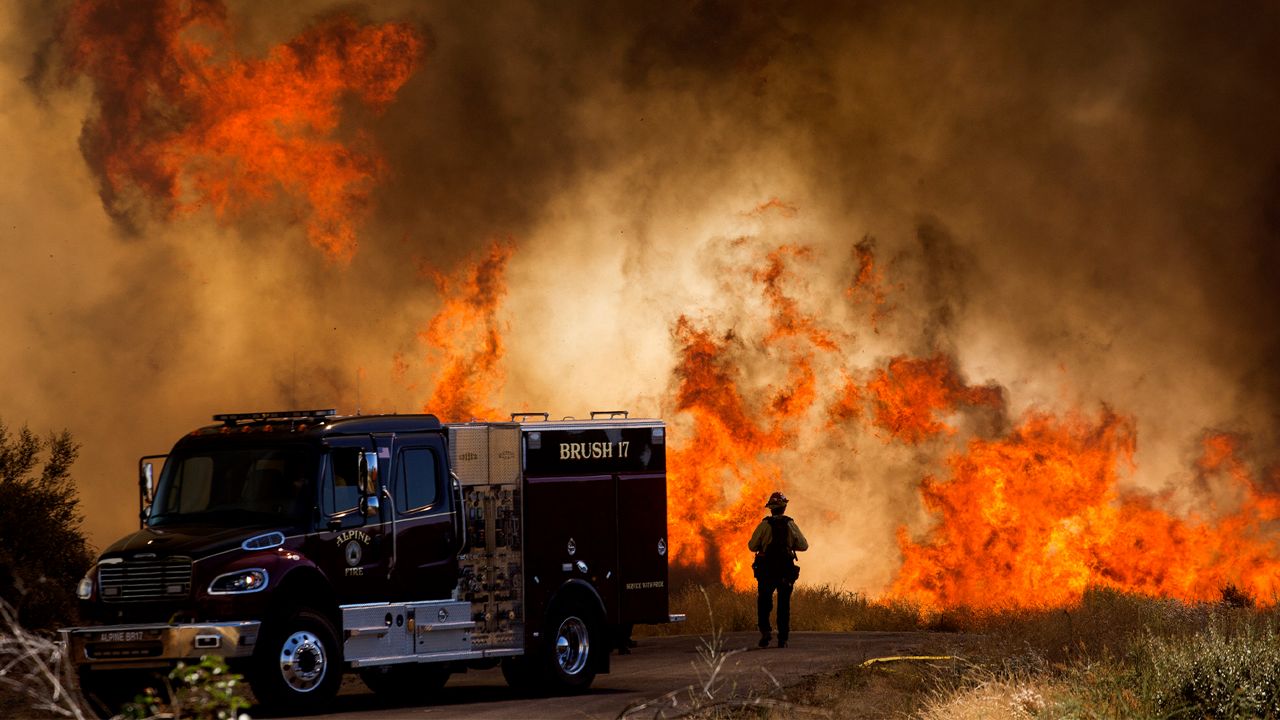 A firefighter stands next to a fire truck as flames flare at the Apple Fire in Cherry Valley, Calif., Saturday, Aug. 1, 2020. The blaze, which is now 30% contained, is extending on a northeast track at roughly mile-high elevations in the area of Millard Canyon, according to the U.S. Forest Service. An estimated 28,085 acres have burned. (AP Photo/Ringo H.W. Chiu)