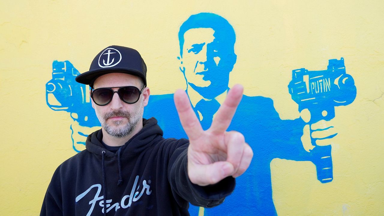 Street artist Todd Goodman, known as 1GoodHombre, stands in front of his stencil of Ukrainian President Volodymyr Zelenskyy holding submachine guns, painted without a permit on a building's wall in Santa Monica, Calif., on Monday, March 21, 2022. (AP Photo/Eugene Garcia)