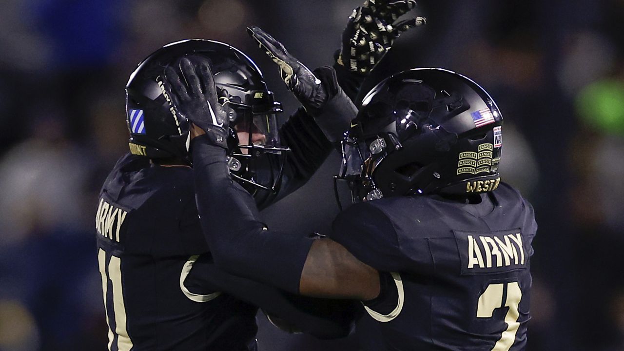 two army football players, in all-black uniforms, celebrate together after a play