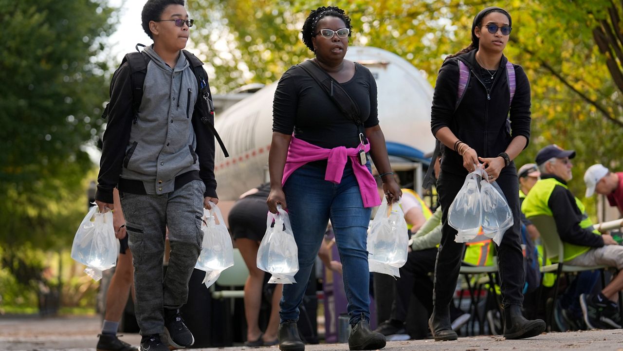 People carry bags of fresh water after filling up at a distribution site in the aftermath of Hurricane Helene on Wednesday, Oct. 2, 2024, in Asheville, N.C. (AP Photo/Jeff Roberson)