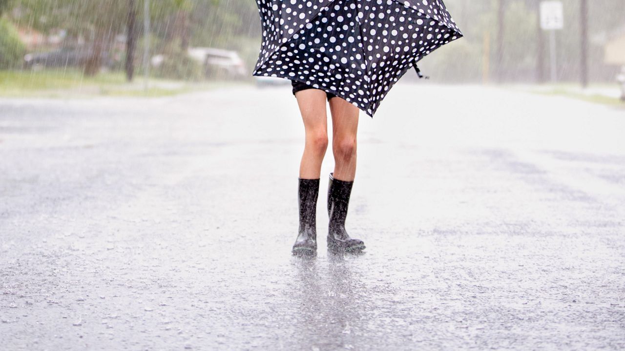 Ten-year-old girl with a black and white polka-dotted umbrella, black rain boots, in a residential street during a rainstorm. (Getty Images)