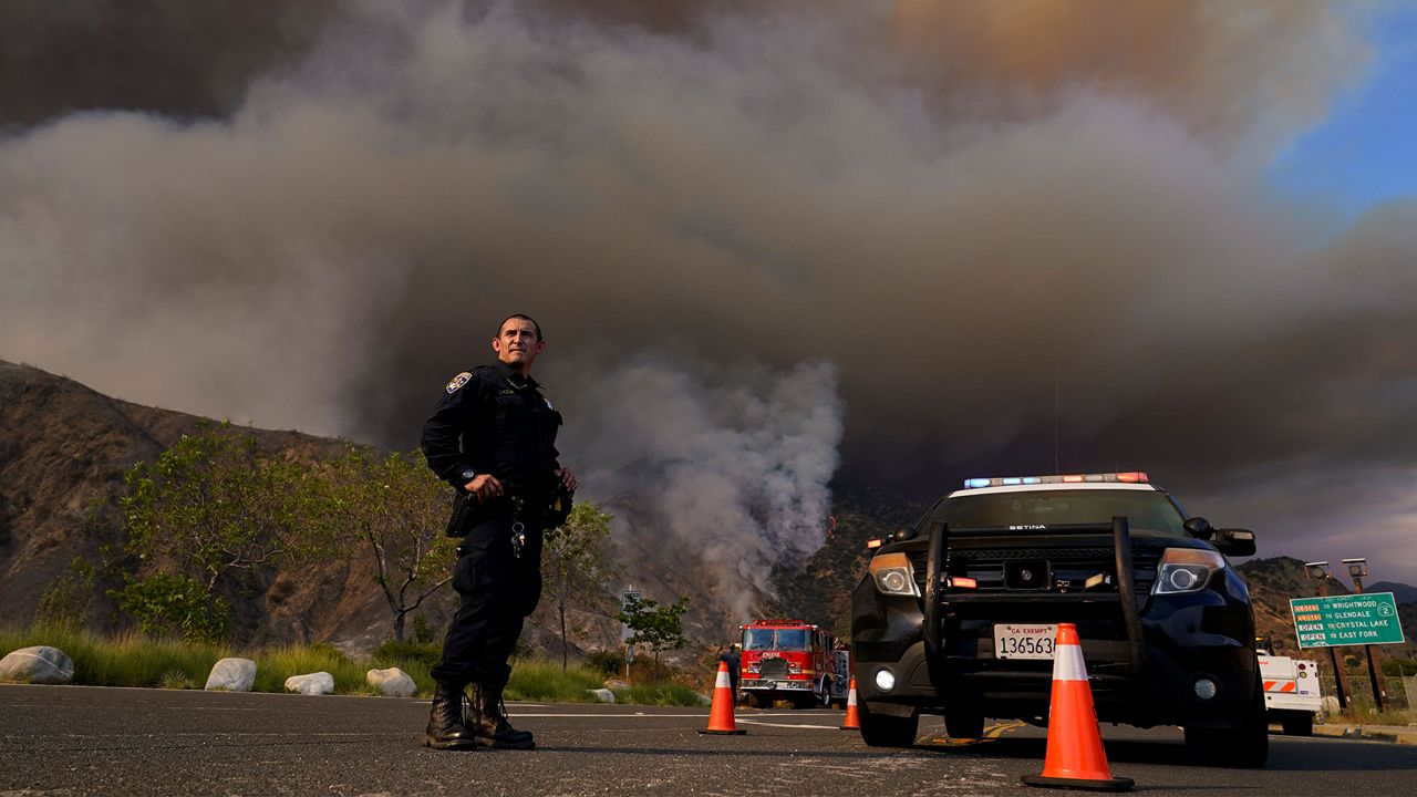 A highway patrolman stands at a road closure in front of the Ranch Fire, Thursday, Aug. 13, 2020, in Azusa, Calif. Heat wave conditions were making difficult work for fire crews battling brush fires and wildfires across Southern California on Thursday. (AP Photo/Marcio Jose Sanchez)