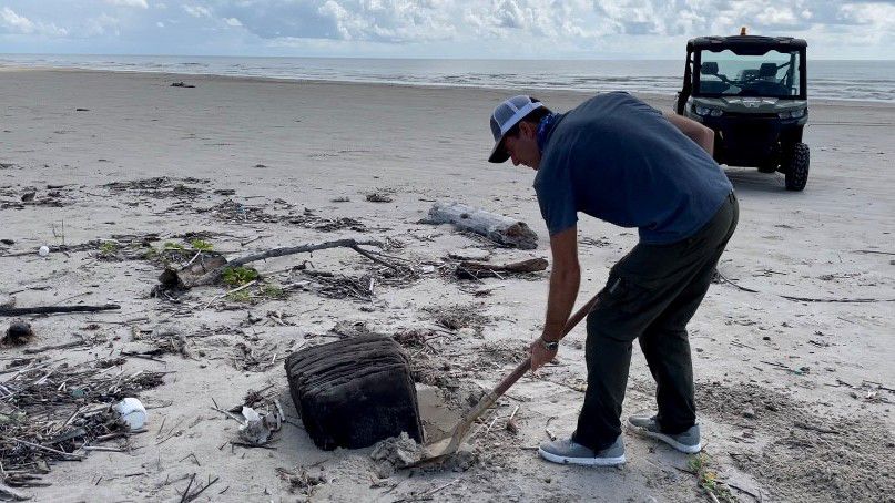 Marine biologist Jace Tunnell survey's a rubber bail that washed up on the Texas shore in this image from August 2021. (Spectrum News 1/Crystal Dominguez)
