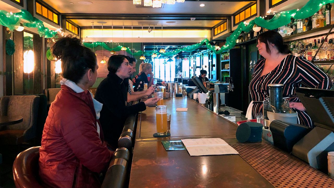 Patrons Maria Moreno, far left, and Aundra Herman, second from left, talk to bartender Felicity Gibbs, right, at "Here & Now" in the Arts District in Los Angeles Sunday, March 15, 2020. California Gov. Gavin Newsom is calling for all bars, wineries, nightclubs and brewpubs to close in the nation's most populous state. Also Sunday, he urged seniors and people with chronic health conditions to isolate themselves at home in a bid to contain the spread of the coronavirus. Newsom says the state will reduce occupancy in restaurants by half to keep people farther away from each other. (AP Photo/Stefanie Dazio)