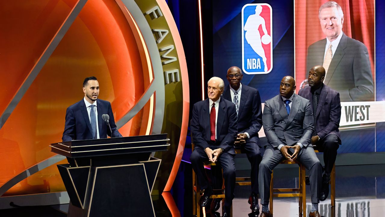 Jonnie West, left, speaks during his late father Jerry West's enshrinement in the Basketball Hall of Fame as, from second from left to right, Pat Riley, Bob McAdoo, Magic Johnson and James Worthy look on Sunday in Springfield, Mass. (AP Photo/Jessica Hill)