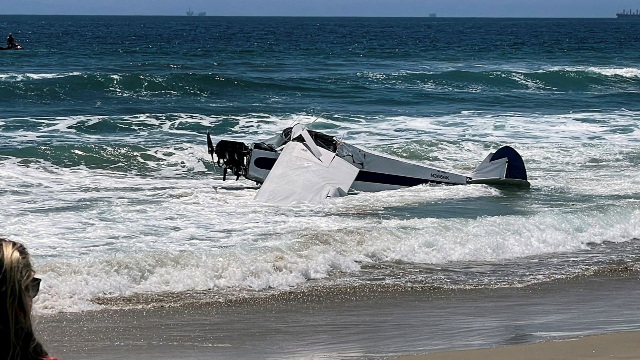 A small plane sits in the surf after it crashed into the ocean just off Huntington Beach, Calif. on Friday, July 22, 2022, during a lifeguarding competition. (Corinne Baginski via AP)