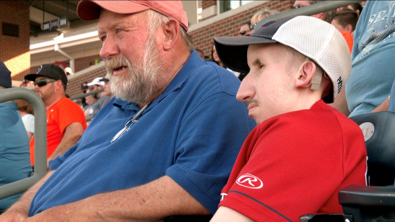 Benjamin’s father Mark, left, tells Benjamin who is up to bat during DBU’s non-conference game against No. 3 Oklahoma State. (Spectrum News 1/Robbie Fuelling)