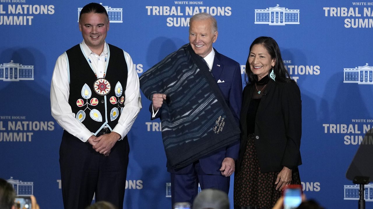 Interior Secretary Deb Haaland, right, and Bryan Newland, Assistant Secretary for Indian Affairs at the Department of the Interior, left, present President Joe Biden with an Eighth Generation blanket from a tribally-owned business, embroidered with "Joe Biden Champion for Indian Country," at the 2024 White House Tribal Nations Summit at the Department of the Interior in Washington, Monday, Dec. 9, 2024. (AP Photo/Susan Walsh)