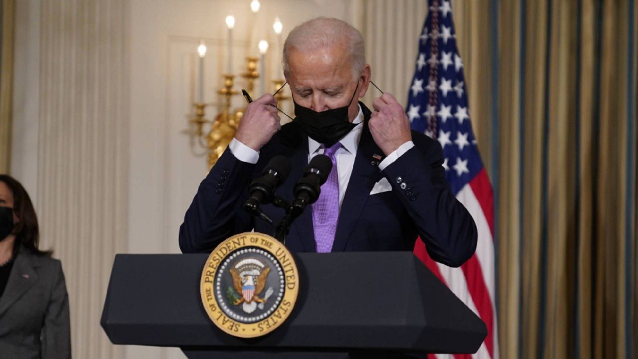 President Joe Biden removes his face mask before speaking in the State Dining Room of the White House, Tuesday, Jan. 26, 2021, in Washington. (AP Photo/Evan Vucci)