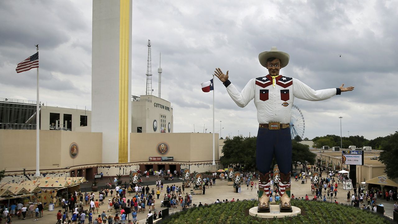 The Tower Building and the Cotton Bowl Stadium can be seen behind visitors to the fair ground as they walk around after an official ceremony welcoming back Big Tex, Friday, Sept. 27, 2013, in Dallas. (AP Photo/Tony Gutierrez)