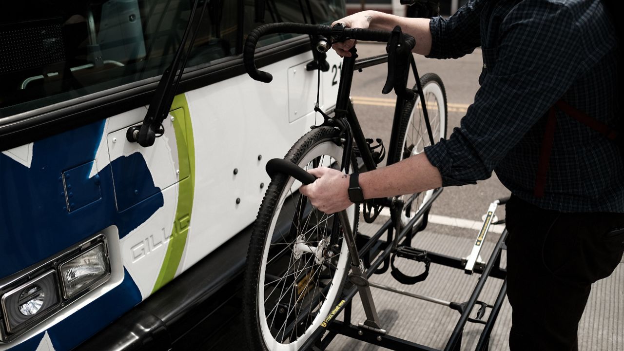 A person loads a bike onto a rack on the front of a Cincinnati Metro bus.