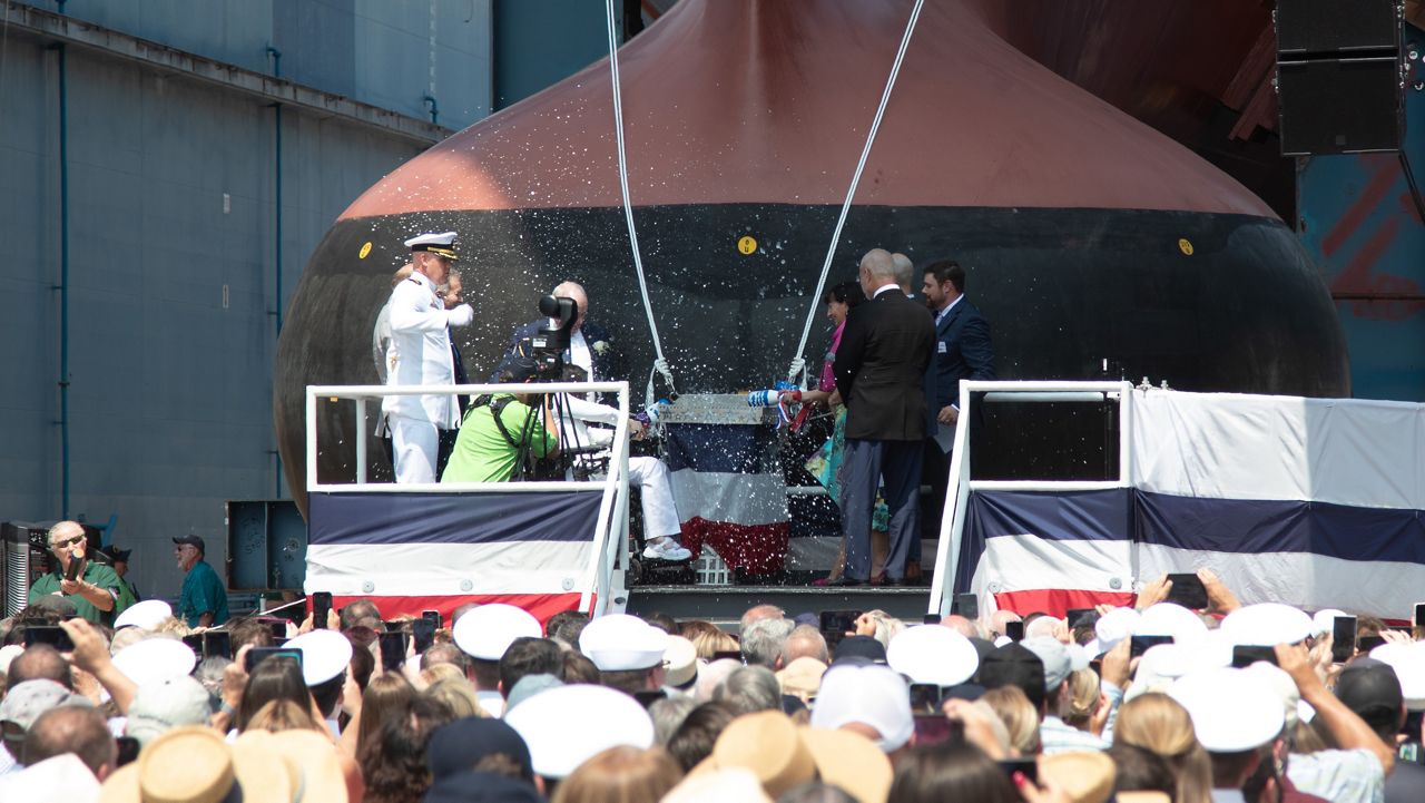 Sisters Teresa Gallagher Keegan, Pauline Gallagher and Rosemarie Gallagher break bottles of sparkling wine over the bow of a destroyer that will bear the name of their brother, Patrick Gallagher, Saturday at Bath Iron Works. The three sisters traveled to Maine from Ireland this week for the ceremony. (Photo courtesy BIW)