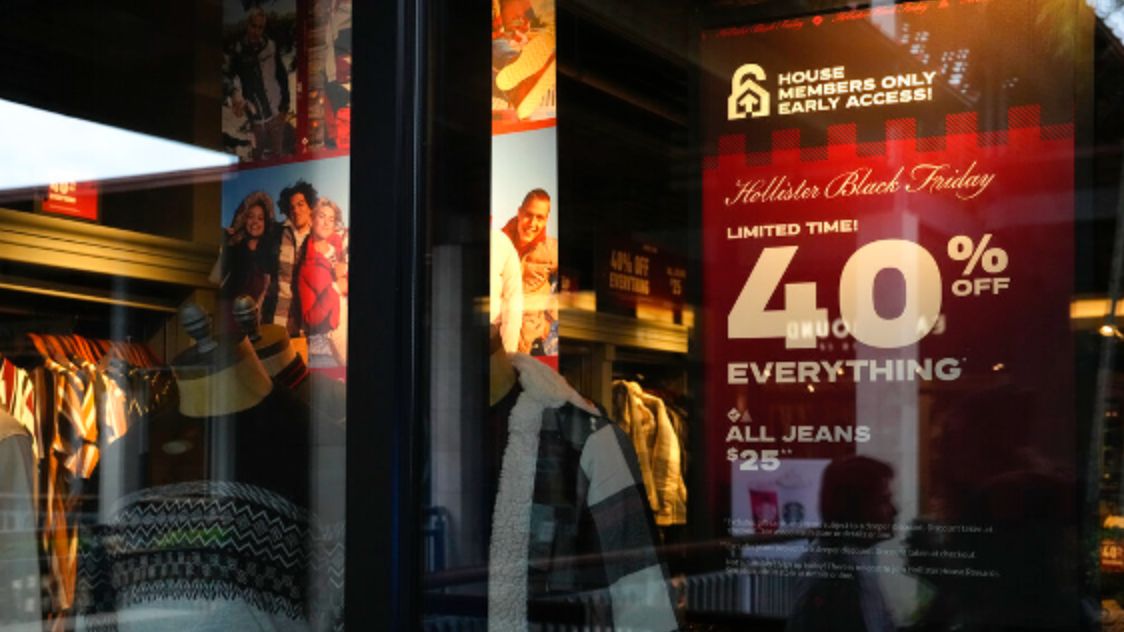 The reflections of passing shoppers are seen in the glass of a Hollister clothing store advertising sales, ahead of Black Friday and the Thanksgiving holiday, Monday, Nov. 21, 2022, in Miami. Retailers are ushering in the start of the holiday shopping season on the day after Thanksgiving, preparing for the biggest crowds since 2019. (AP Photo/Rebecca Blackwell)
