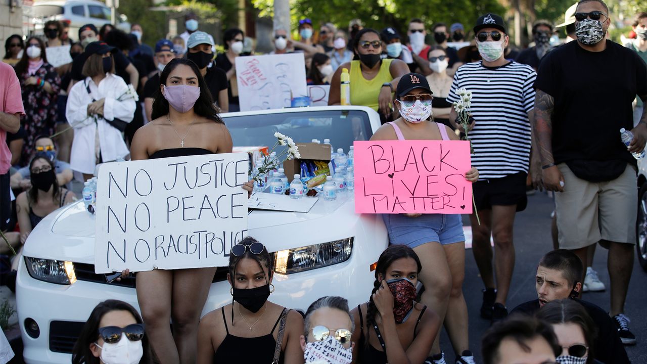 Demonstrators hold signs on Sunset Blvd. Tuesday, June 9, 2020, in Los Angeles during a sit-in protest over the death of George Floyd who died May 25 after he was restrained by Minneapolis police. (AP Photo/Marcio Jose Sanchez)
