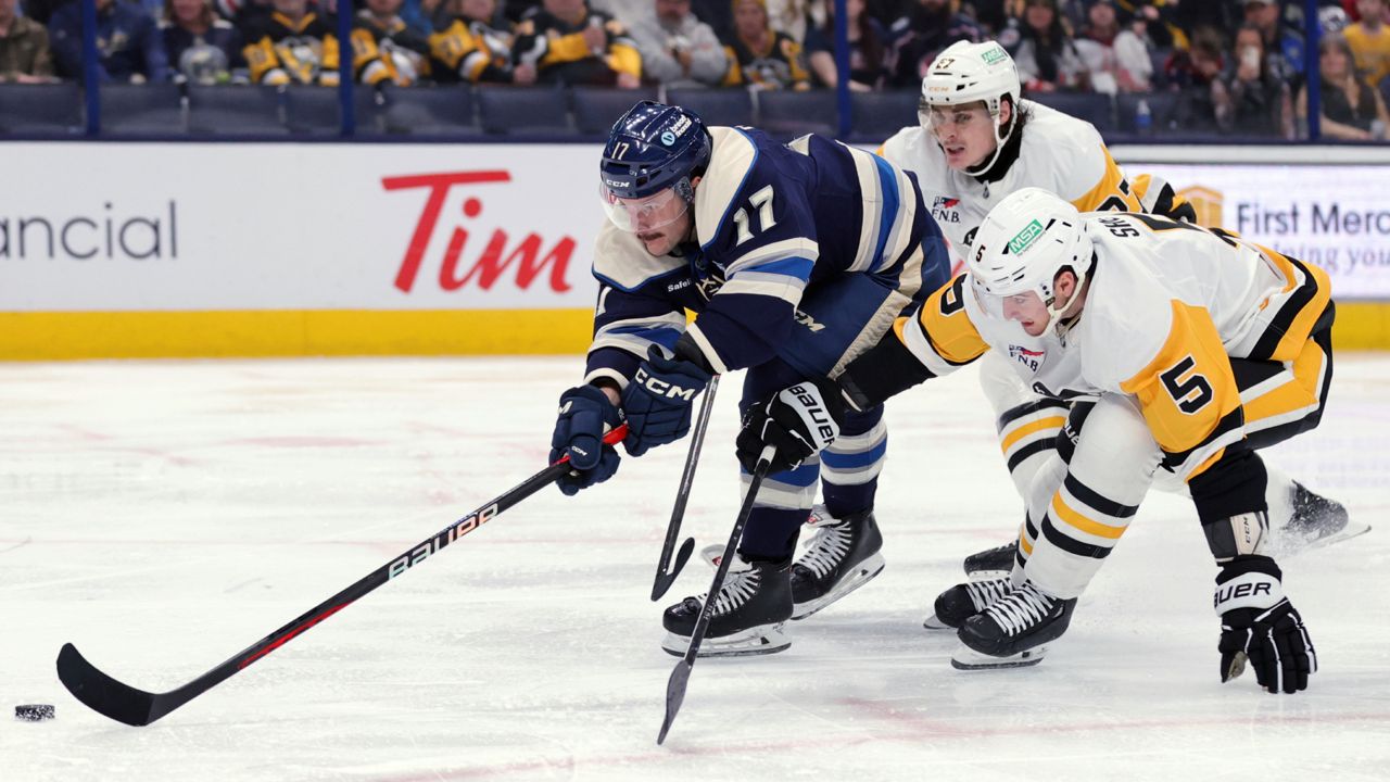 Columbus Blue Jackets forward Justin Danforth, left, reaches for the puck in front of Pittsburgh Penguins defenseman Ryan Graves, center, and defenseman Ryan Shea during the second period of an NHL hockey game in Columbus, Ohio, Friday, Nov. 15, 2024.