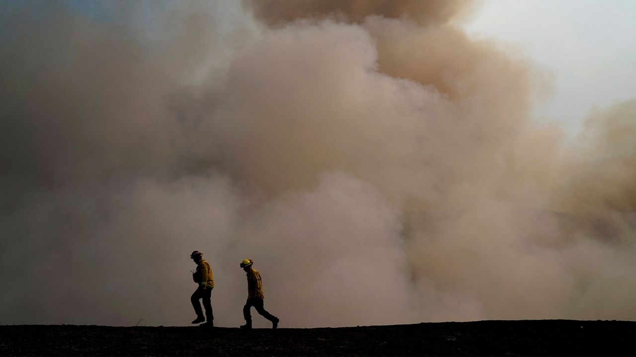 Two firefighters walk along the ridge as smoke from the Blue Ridge Fire rises Tuesday, Oct. 27, 2020, in Yorba Linda, Calif. (AP Photo/Jae C. Hong)