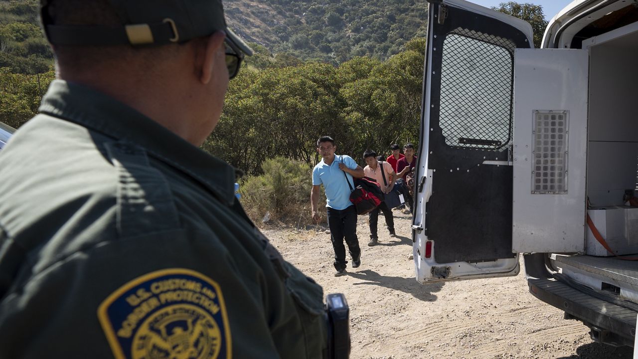 A Border Patrol agent leads a group of migrants seeking asylum toward a van to be transported and processed, Wednesday, June 5, 2024, near Dulzura, Calif. (AP Photo/Gregory Bull)