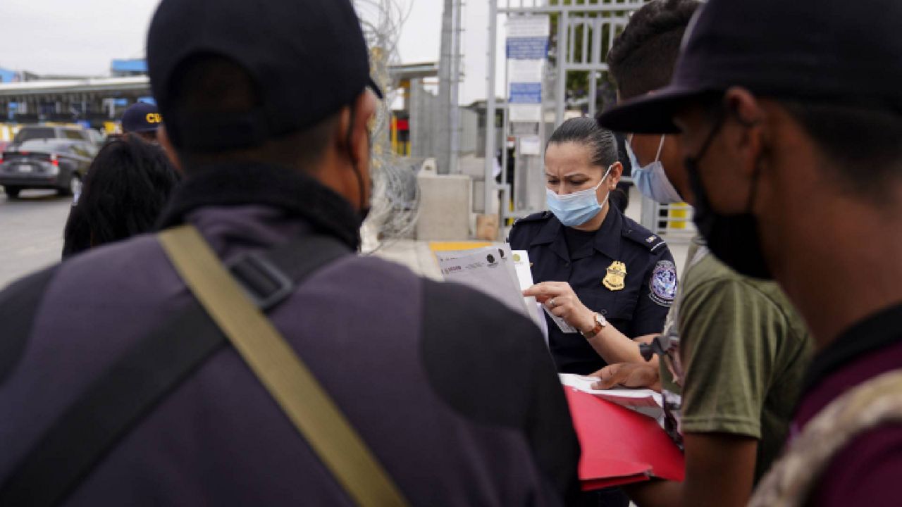 A United States Customs and Border Protection officer examines paperwork of migrants waiting to cross into the United States to begin the asylum process Monday, July 5, 2021, in Tijuana, Mexico. (AP Photo/Gregory Bull)