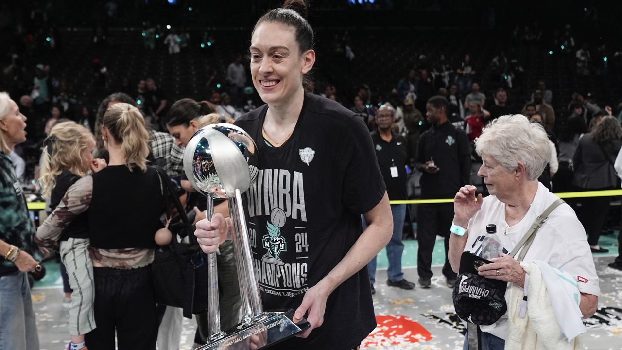 breanna stewart holds championship trophy, wearing a wnba championship shirt