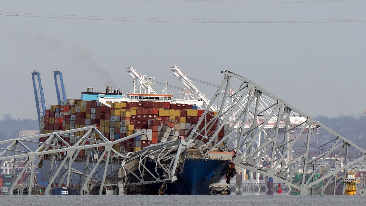 A helicopter flies over a container ship as it rests against wreckage of the Francis Scott Key Bridge on Tuesday, March 26, 2024, as seen from Pasadena, Md. (AP Photo/Mark Schiefelbein)