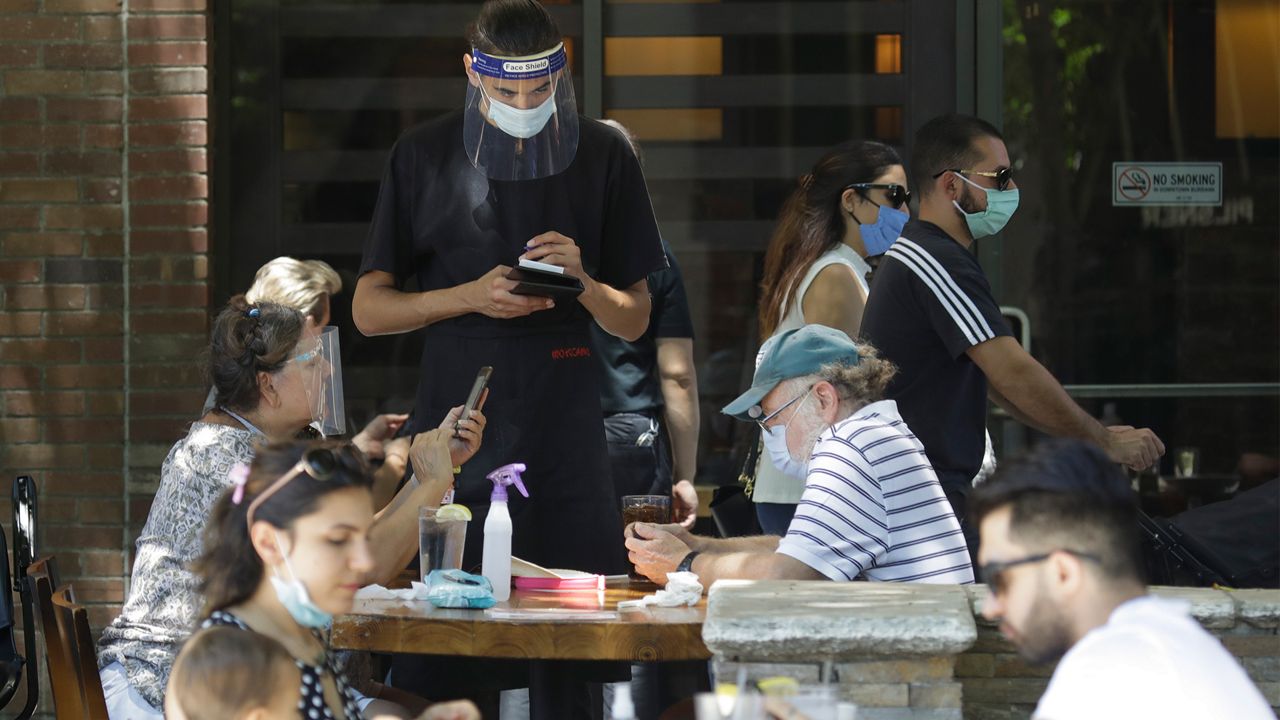 A waiter takes a food order Saturday, July 18, 2020, in Burbank, Calif. The city of Burbank has closed off some streets in the downtown district to allow restaurants to expand their outdoor seating arrangements amid the Coronavirus pandemic. (AP Photo/Marcio Jose Sanchez)
