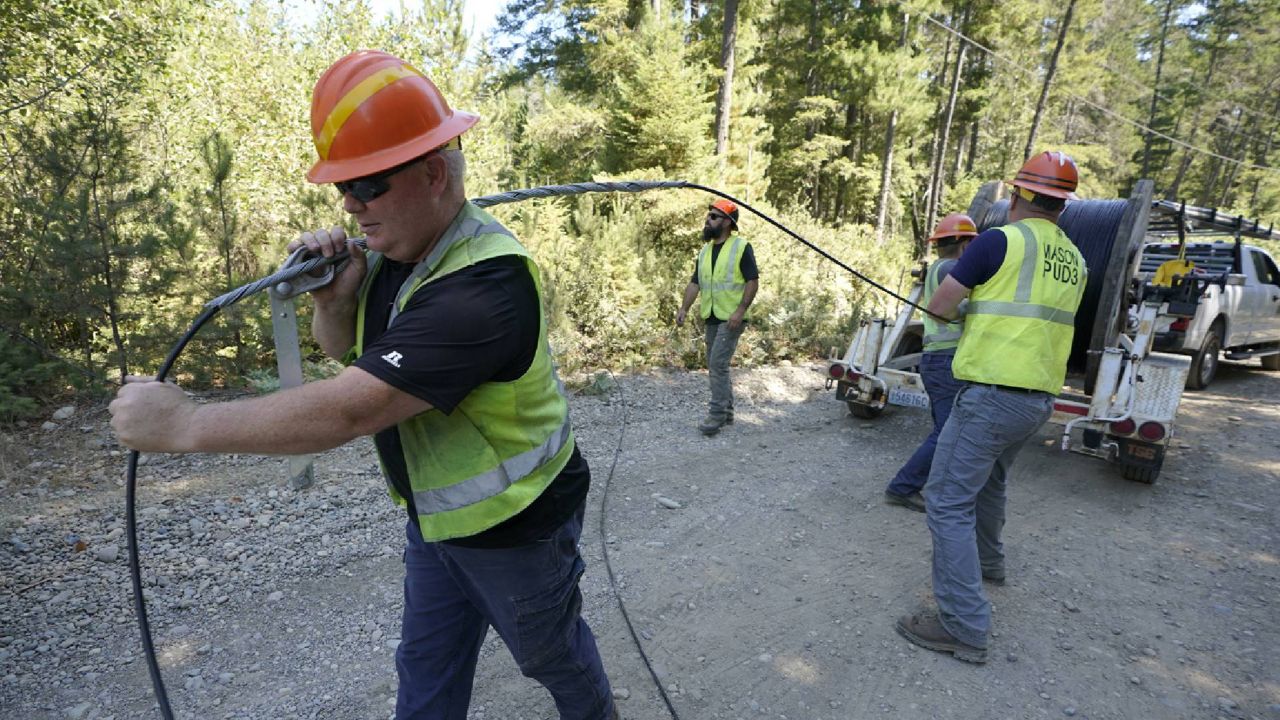 In this Wednesday, Aug. 4, 2021, file photo, Carl Roath, left, a worker with the Mason County (Wash.) Public Utility District, pulls fiber optic cable off of a spool, as he works with a team to install broadband internet service to homes in a rural area surrounding Lake Christine near Belfair, Wash. (AP Photo/Ted S. Warren, File)