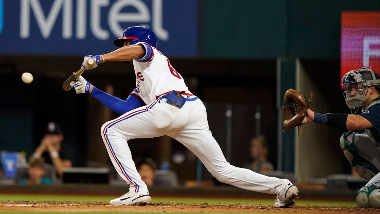 Texas Rangers' Bubba Thompson, left, hits a sacrifice bunt in front of Seattle Mariners catcher Cal Raleigh during the fourth inning of a baseball game in Arlington, Texas, Saturday, Aug. 13, 2022. Rangers' Charlie Culberson scored on the play. (AP Photo/LM Otero)