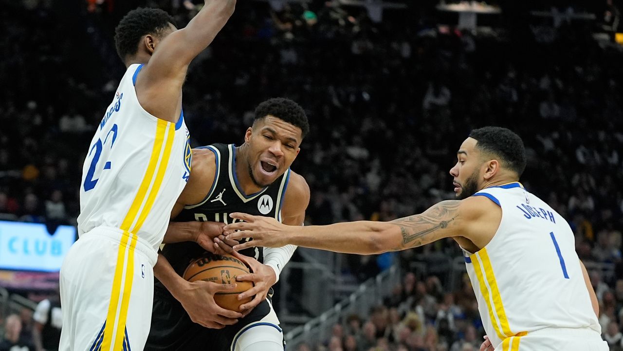 Milwaukee Bucks' Giannis Antetokounmpo is fouled as he drives between Golden State Warriors' Andrew Wiggins and Cory Joseph