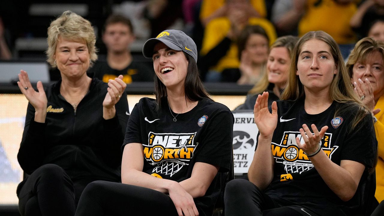 Iowa guard Caitlin Clark, center, sits with coach Lisa Bluder, left, and guard Kate Martin, right, as she finds out her number will be retired, during an Iowa women's basketball team celebration Wednesday, April 10, 2024, in Iowa City, Iowa. Iowa lost to South Carolina in the college basketball championship game of the women's NCAA Tournament on Sunday. (AP Photo/Charlie Neibergall)