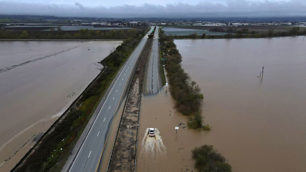 A CalTrans vehicle drives north through floodwaters that closed state Highway 1 at the Santa Cruz County line, in California, Sunday, March 12, 2023. (Shmuel Thaler/The Santa Cruz Sentinel via AP)