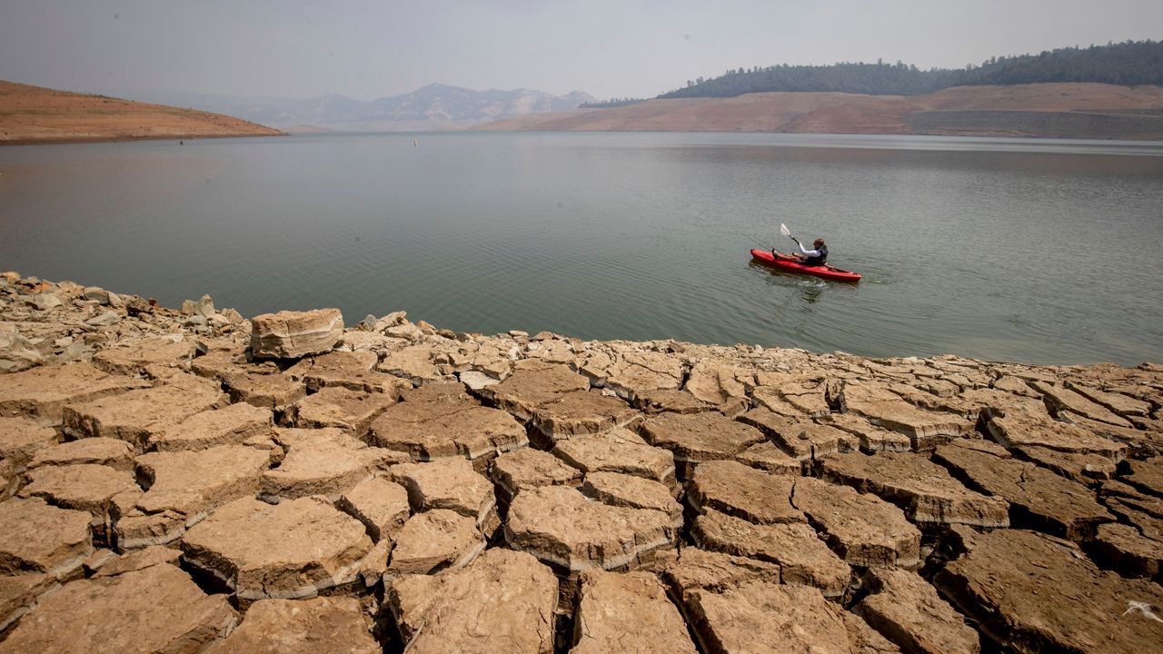 In this Aug. 22, 2021, file photo, a kayaker fishes in Lake Oroville as water levels remain low due to continuing drought conditions in Oroville, Calif. (AP Photo/Ethan Swope)
