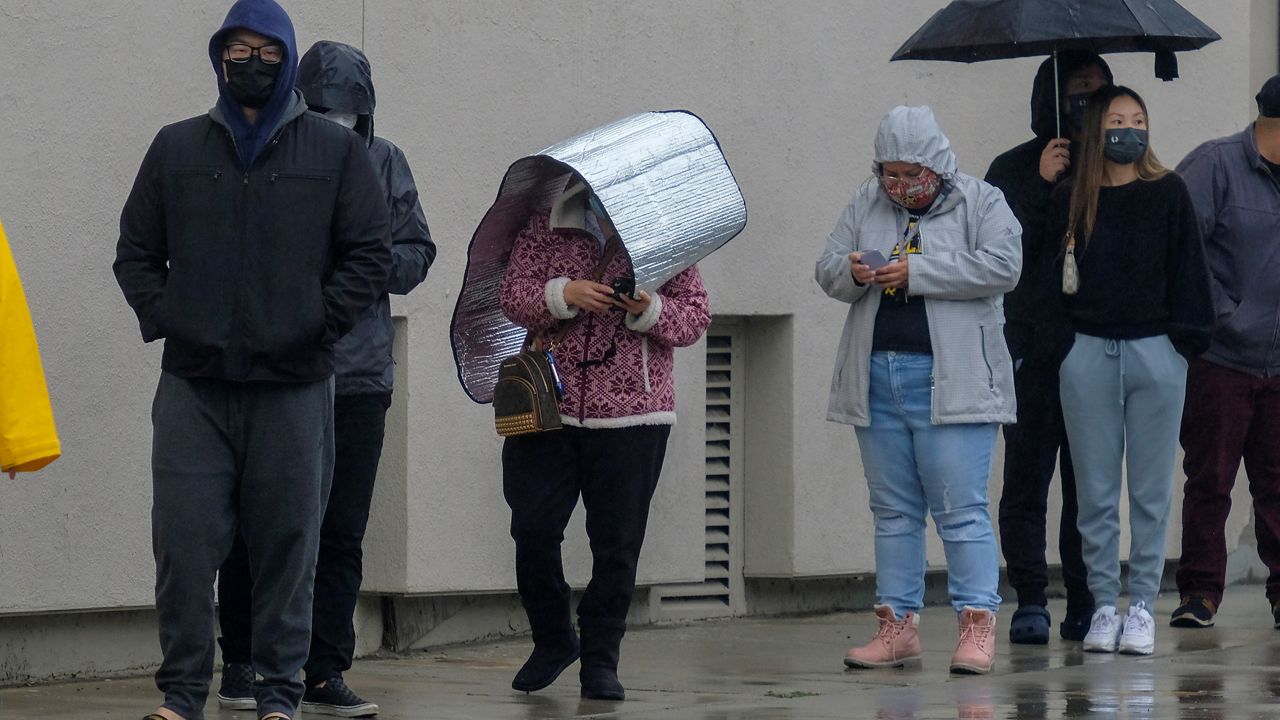 People with umbrellas wait in line for a free COVID-19 test outside Lincoln Park Recreation Center in Los Angeles on Thursday, Dec. 23, 2021. (AP Photo/Ringo H.W. Chiu)