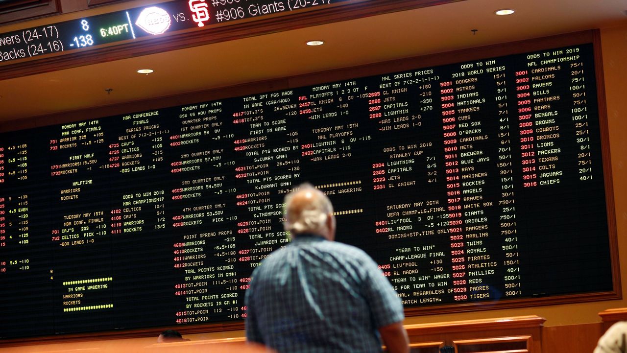 man looks at a screen displaying sports betting odds in vegas