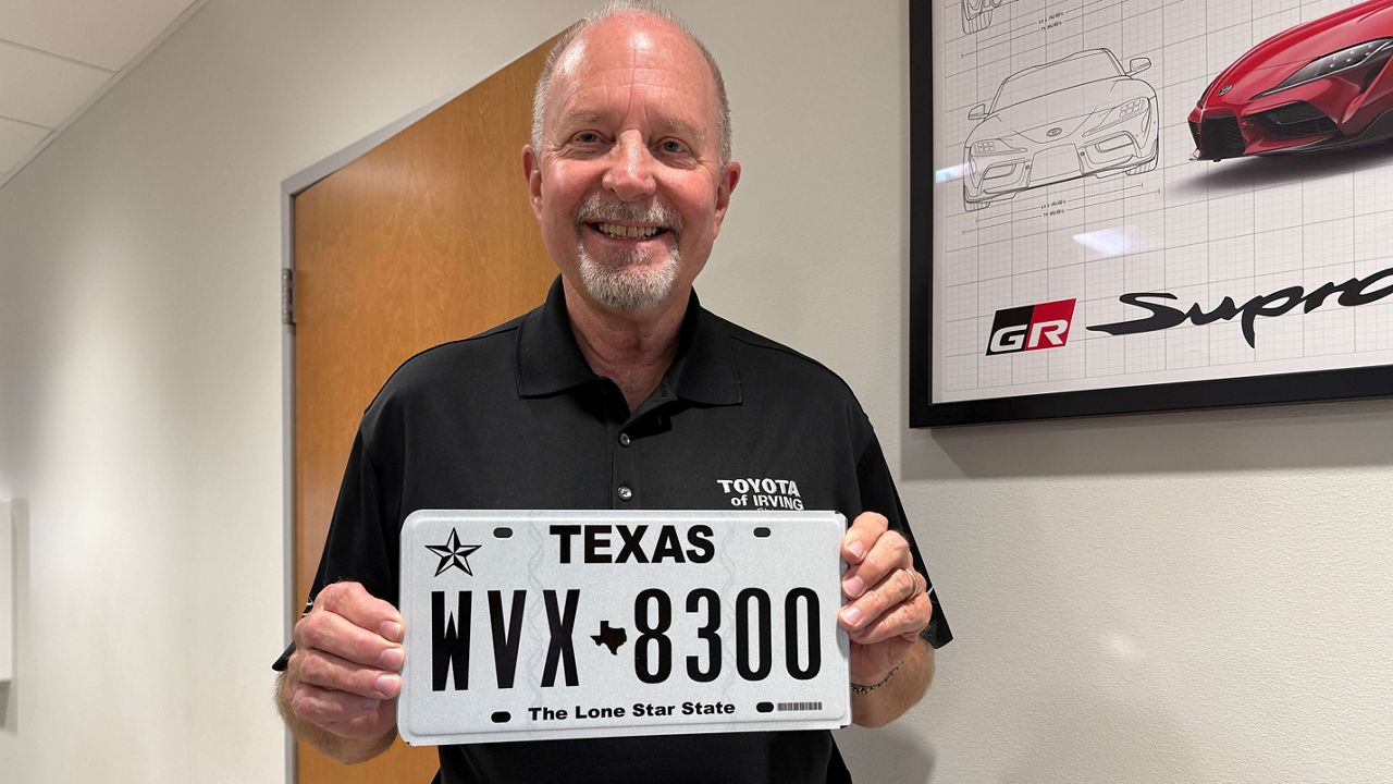 David Schoemaker, president of Toyota of Irving, holds a new metal car plate at his dealership. (Spectrum News 1/Blessing Iwuchukwu)