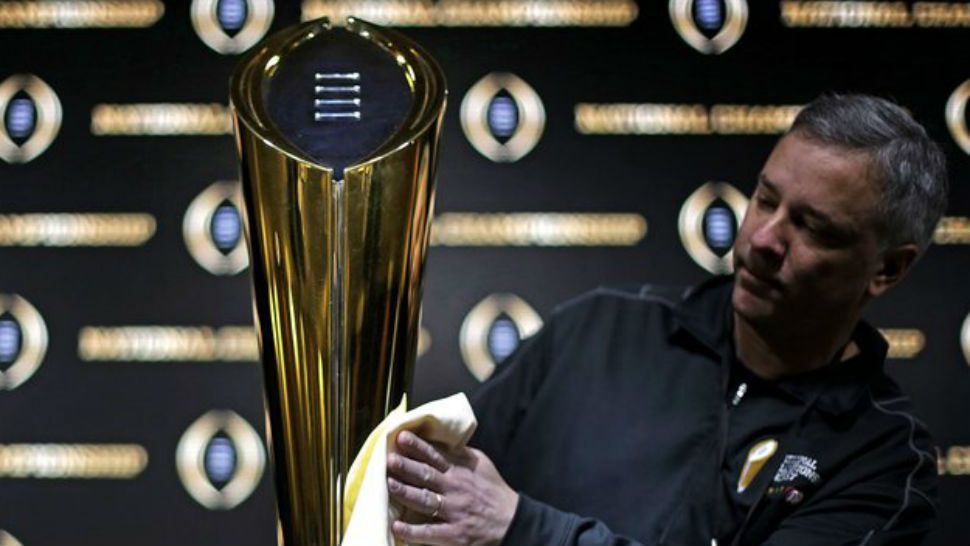 FILE - In this Jan. 7, 2018 file photo Charley Green buffs the NCAA college football championship trophy before a coaches news conference in Atlanta. The College Football Playoff selection committee begins its fifth season Tuesday, Oct. 30, 2018 of presenting weekly rankings and if form holds two schools in the first top four will go on to play in the semifinals. The usefulness of the committee’s work and the nationally televised reveal is debatable. But what if anything can be learned from the first four years of CFP rankings? Of the 16 teams the committee ranked in the top four of its initial rankings from 2014-17, half made the playoff. (AP Photo/David Goldman, file)