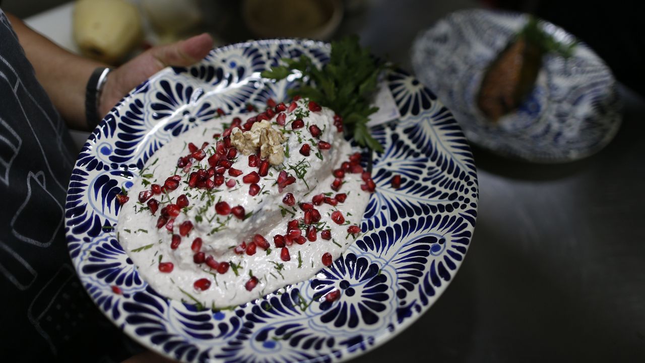 A cook carries out a plate of chiles en nogada to be served to diners at Testal restaurant in downtown Mexico City, Sept. 13, 2019. The recipe was invented in 1821 by a nun, whose name has been lost to history. Agustin de Iturbide, a general in the War of Independence, was the first to taste one. (AP Photo/Rebecca Blackwell, File)