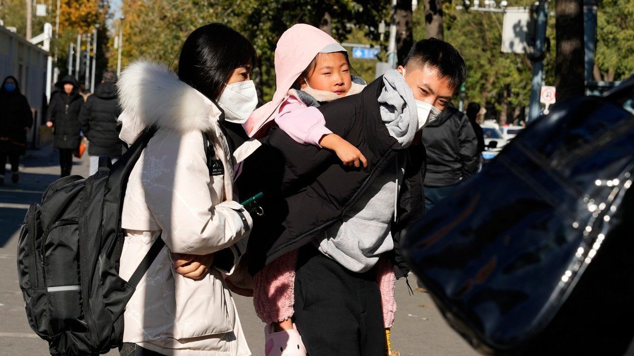 A man carries a child as they leave a children's hospital in Beijing on Nov. 24, 2023. (AP/Ng Han Guan)