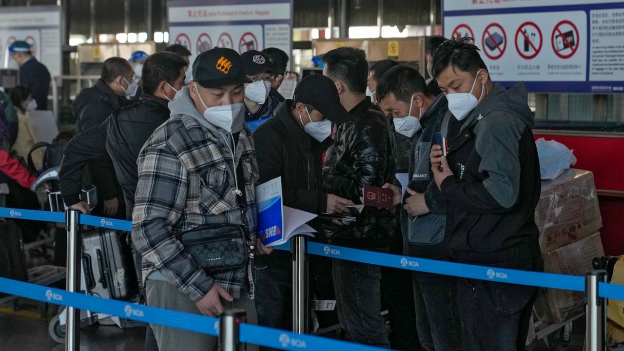 Masked travelers check their passports as they line up Thursday at the international flight check-in counter at the Beijing Capital International Airport. (AP Photo/Andy Wong)