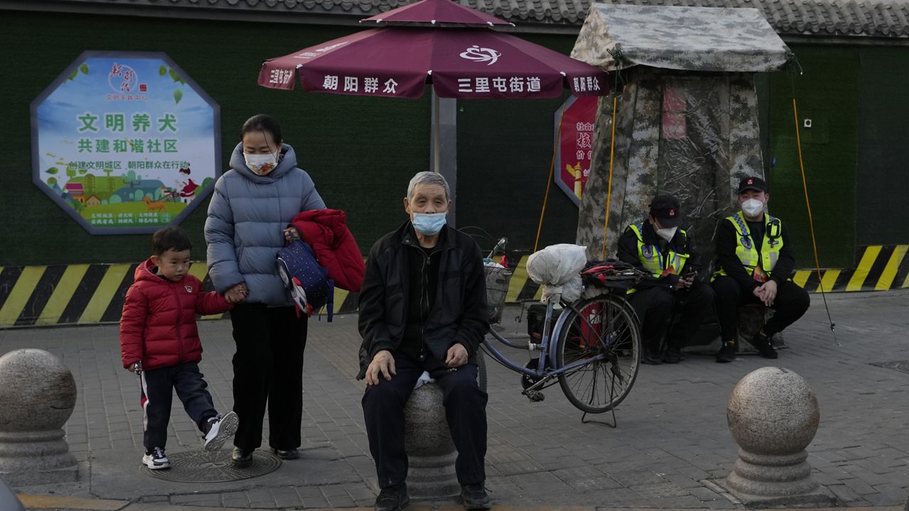 Residents wait to cross a road Monday near members of the Chaoyang militia on duty in Beijing. (AP Photo/Ng Han Guan)