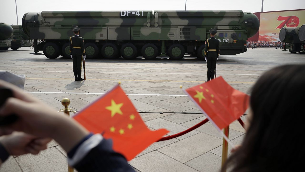 Spectators wave Chinese flags as military vehicles carrying DF-41 nuclear ballistic missiles roll during a parade to commemorate the 70th anniversary of the founding of Communist China in Beijing on Oct. 1, 2019. (AP Photo/Mark Schiefelbein, File)