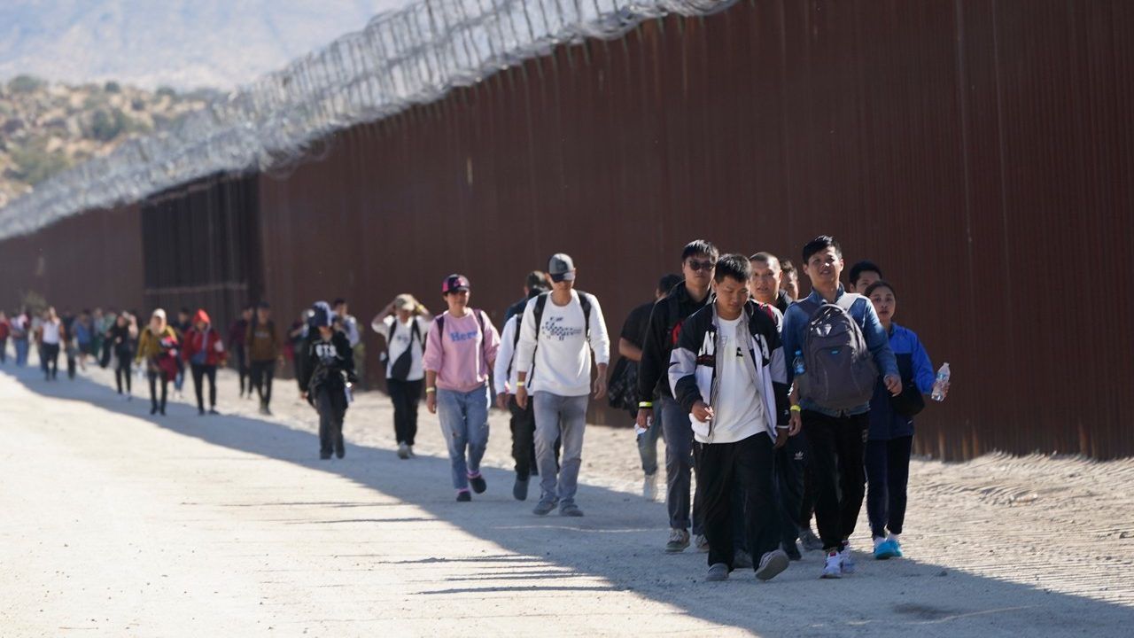 A group of people, including many from China, walk along the wall after crossing the border with Mexico to seek asylum Tuesday near Jacumba, Calif. (AP Photo/Gregory Bull)