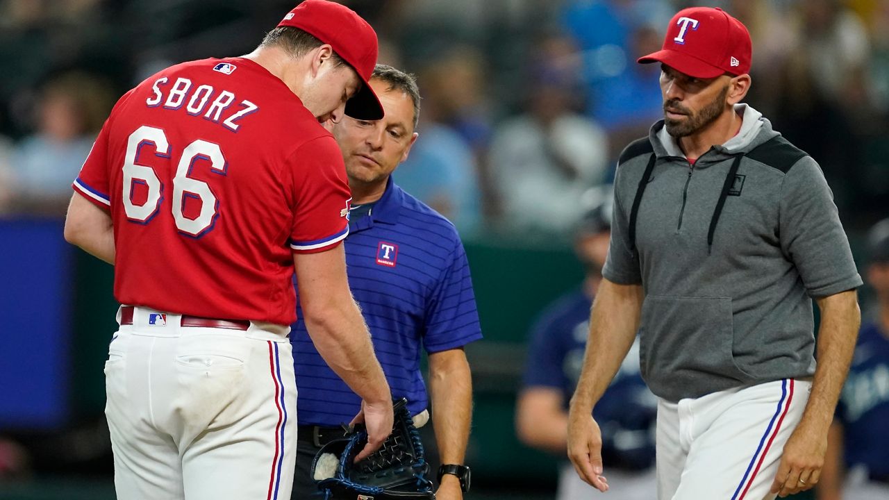 Texas Rangers starting pitcher Josh Sborz (66) is checked on by athletic trainer Matt Lucero, center, and manager Chris Woodward after Sborz was struck by the ball on a single by Seattle Mariners' Mitch Haniger during the first inning of a baseball game in Arlington, Texas, Friday, Aug. 12, 2022. (AP Photo/Tony Gutierrez)
