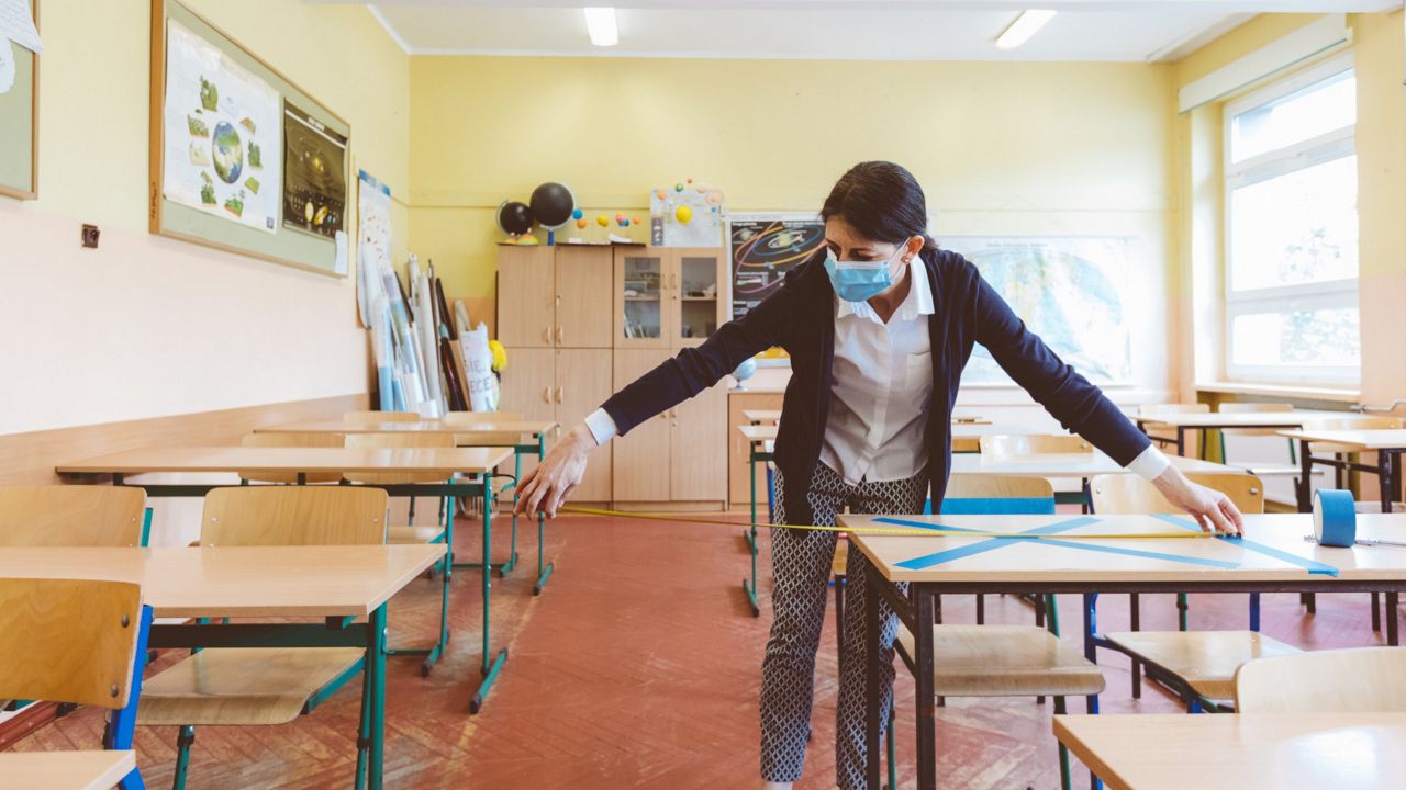 An image of a person measuring distance between classroom desks (Spectrum News/File)