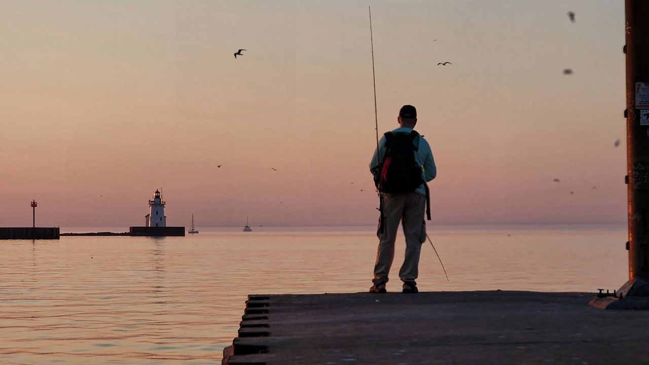 A man fishes off the pier in Cleveland, Ohio, with Cleveland Harbor West Pierhead Light in the background. (Spectrum News 1/Lydia Taylor)